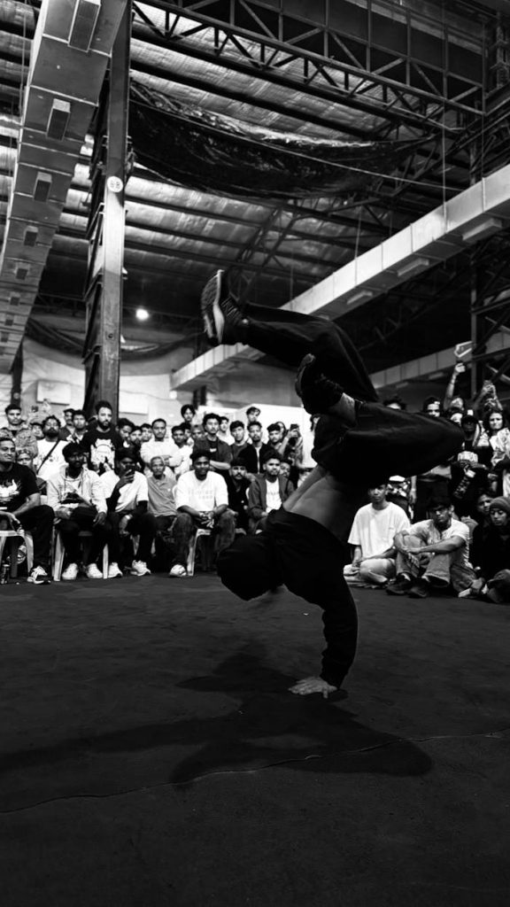Breakdancer performing handstand in front of an engaged crowd in an urban venue.