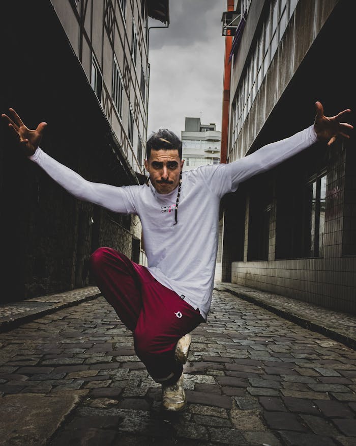 Man in red pants and white shirt performs dance move on cobblestone street.