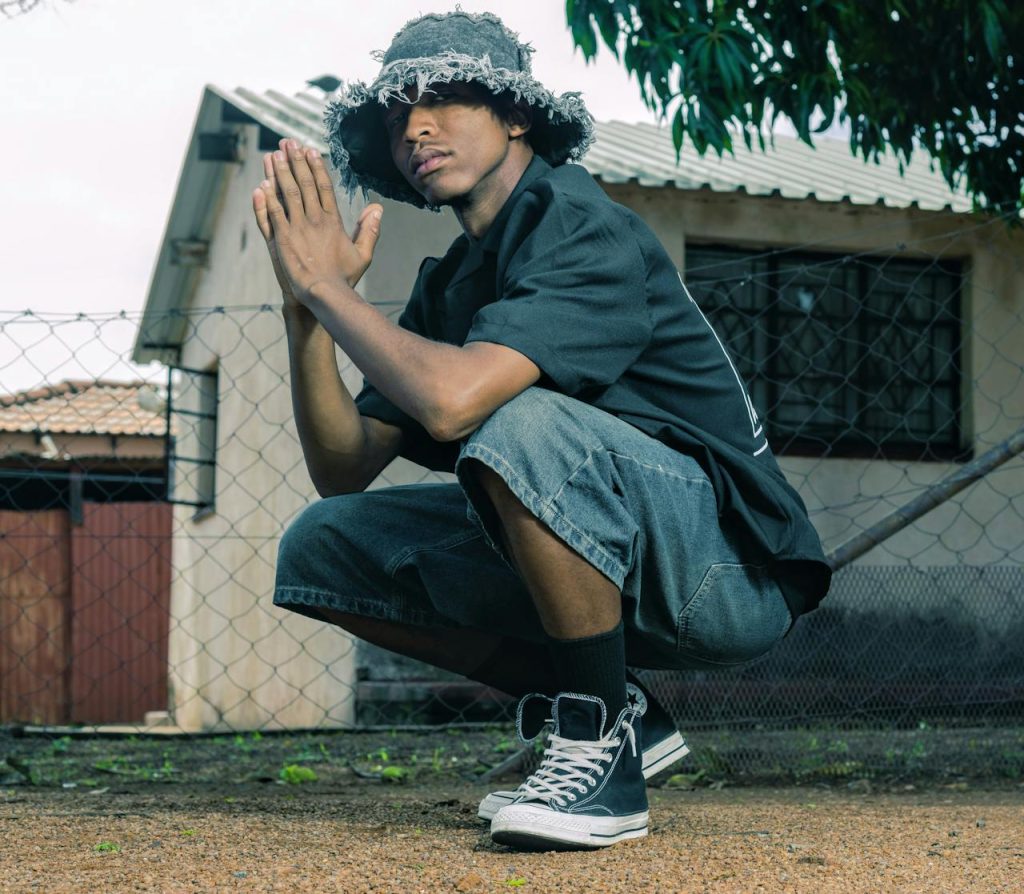 Stylish young man squatting outdoors in casual urban wear, South Africa.